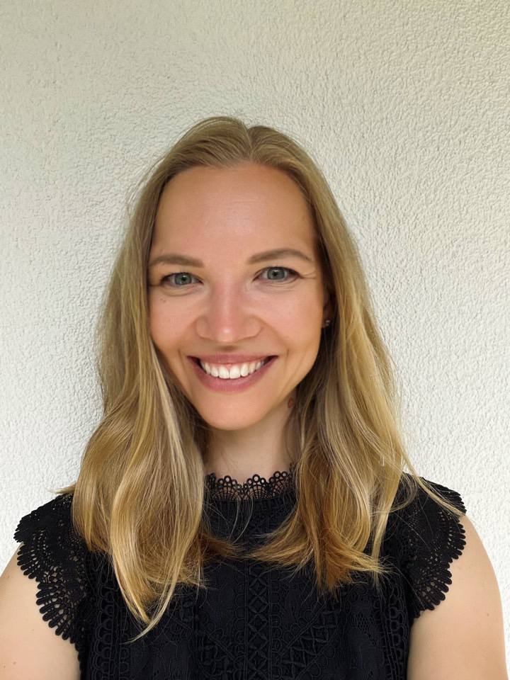 Woman with blonde hair wearing a black top against a white wall