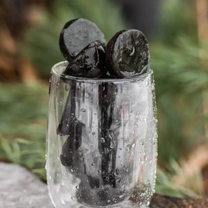 Fresh, frozen spirulina pods in a clear glass with a blurred green background