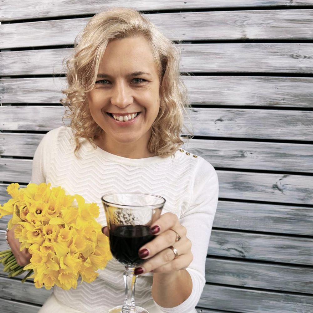 Woman holding a glass of red wine and a bouquet of yellow flowers against a wooden background