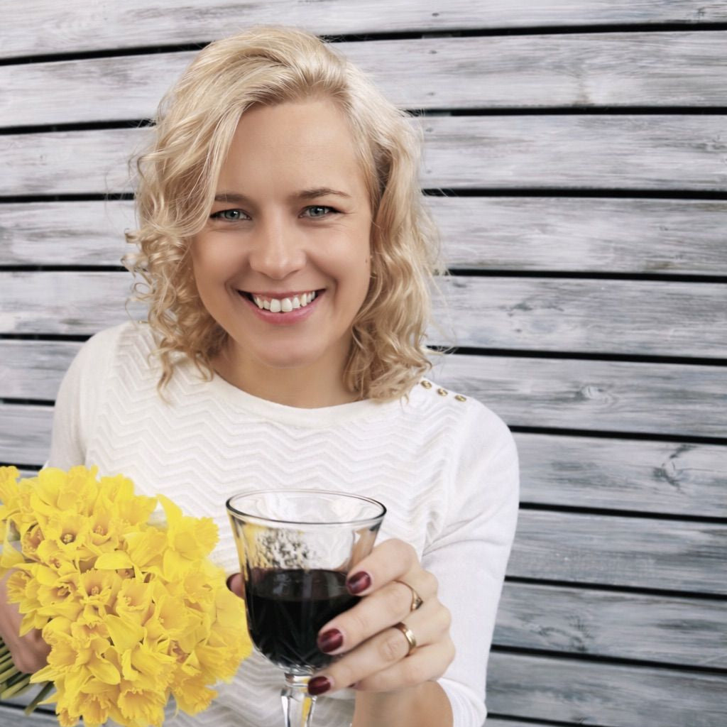 Woman in a white dress holding a glass of spirulina and yellow flowers against a wooden background