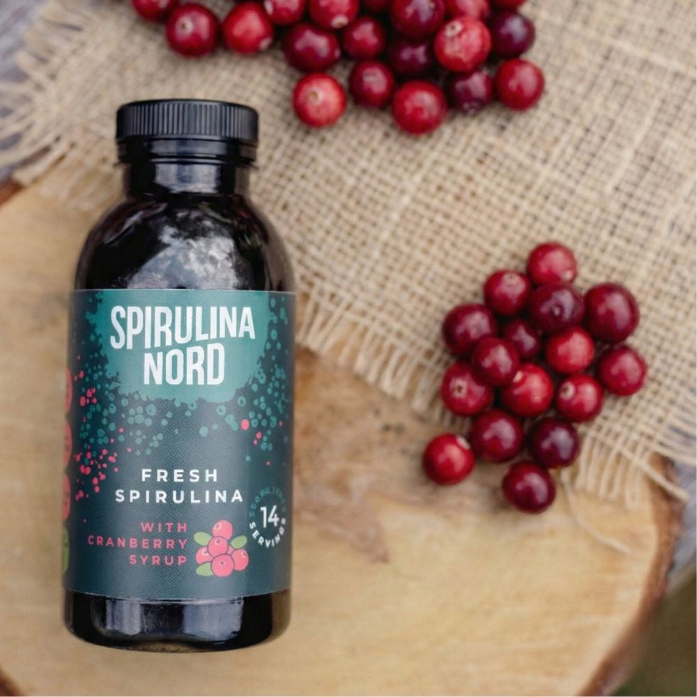SpirulinaNord bottle with cranberries on a wooden surface